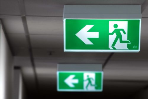 Illuminated green emergency exit signs in hallway ceiling