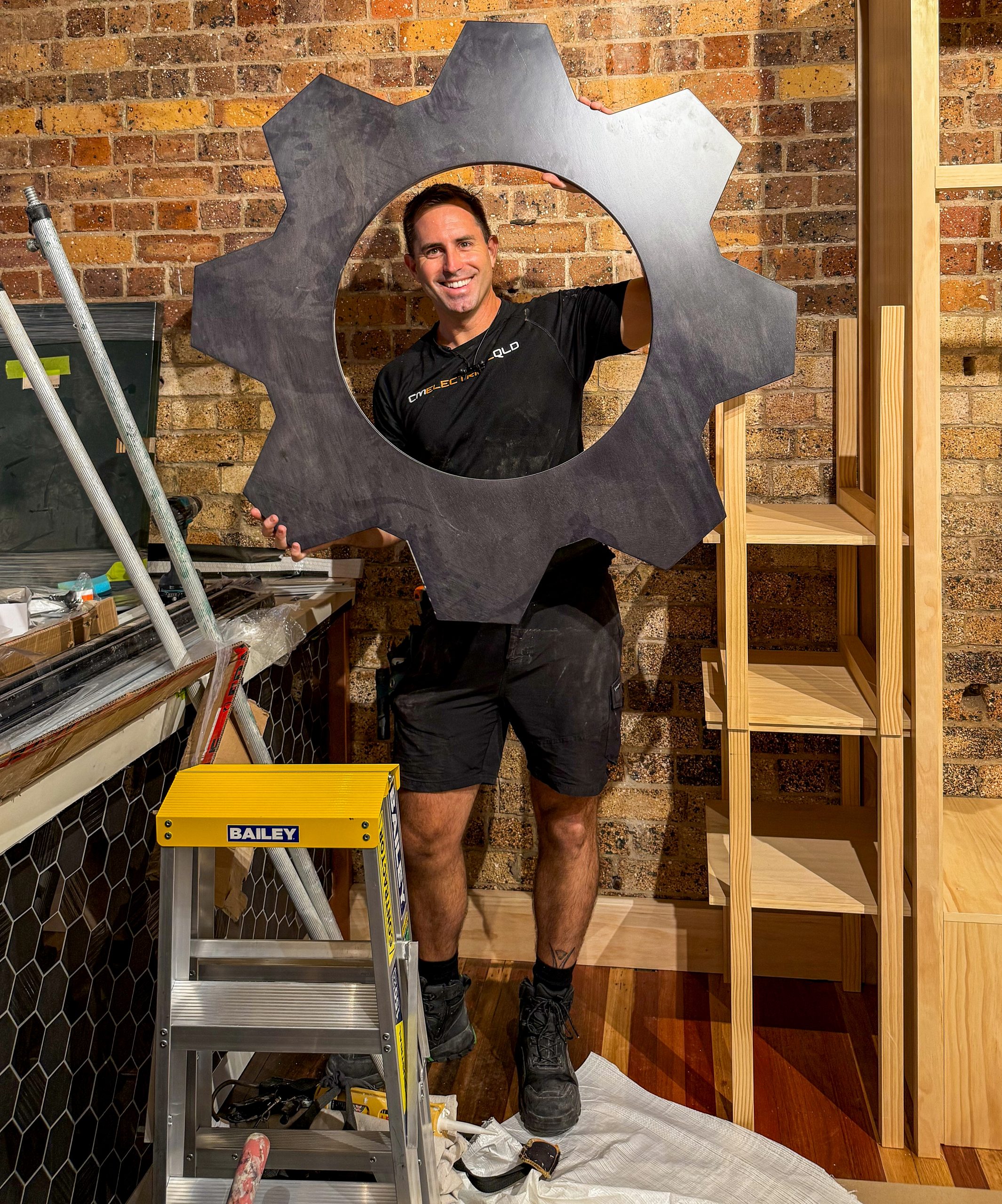 Electrician posing behind large metal gear cutout structure indoors